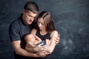 Woman and man holding a newborn. Mom, dad and baby. Close-up. Portrait of  smiling family with newborn on the hands. Happy family on a background. © fadzeyeva