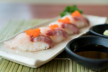 Hamachi sushi on white plate along with Japanese sauce and green leaf decoration, Japanese food, close up at sushi ..
