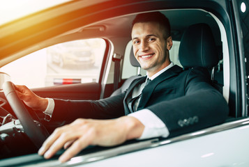 Handsome smiling business man driving a car. Man in fullsuit buying car in dealership