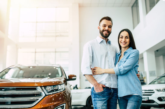 Visit the dealership. Happy young couple chooses and buying a new red car for the family.