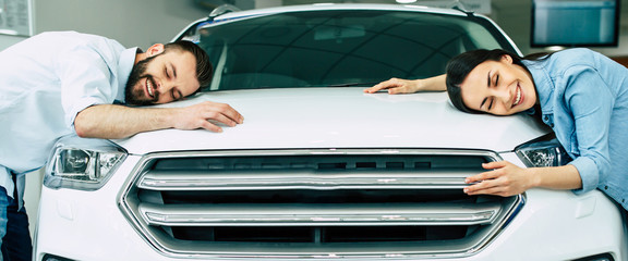 Happy young couple chooses and buying a new car for the family.