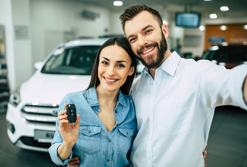 Happy young hugging couple chooses and buying a new car for the family in the dealership.