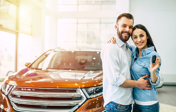 Visit the dealership. Happy young couple chooses and buying a new red car for the family.