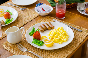 Savoury breakfast meal with scrambled eggs, sausage, tomato and green bean vegetables, watermelon juice.