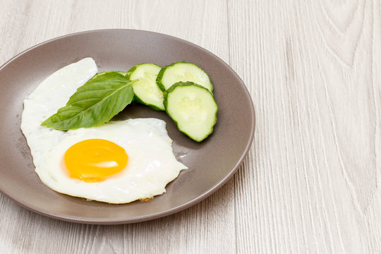 Plate with fried egg, fresh cut cucumber and leaf of basil