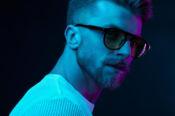 Neon light studio close-up portrait of attractive male model in sunglasses and white t-shirt - 216135905