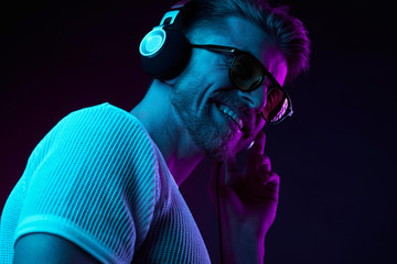 Neon light portrait of bearded smiling man in headphones, sunglasses, white t-shirt. Listening to music - 216136178