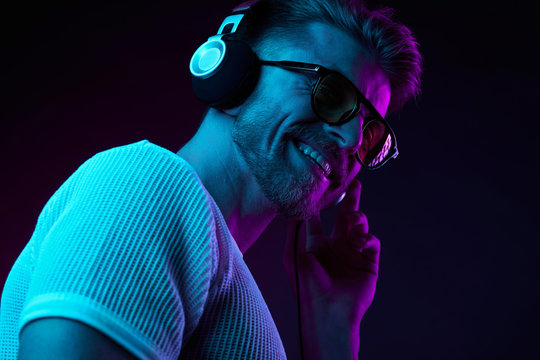 Neon light portrait of bearded smiling man in headphones, sunglasses, white t-shirt. Listening to music