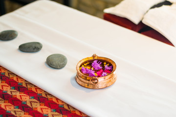 Folded massage towel, flower petals, pebble stones and copper pot on a massage bed in a luxury resort spa, Nepal.