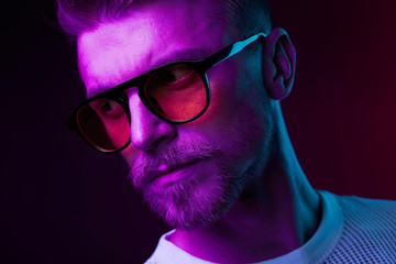 Neon light close-up portrait of serious man with mustaches and beard in orange sunglasses and white t-shirt