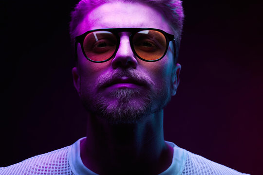 Neon light close-up portrait of serious man model with mustaches and beard in sunglasses and white t-shirt