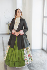 Beautiful woman in green medieval dress and frock-coat near window