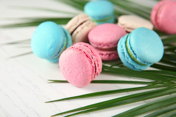 Tasty macarons and palm leaf on light background