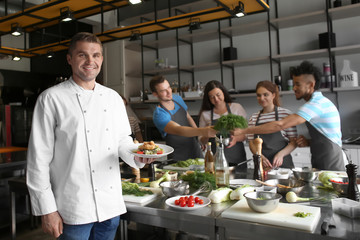 Handsome male chef holding plate with prepared dish during cooking classes