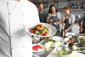 Male chef holding plate with prepared dish during cooking classes