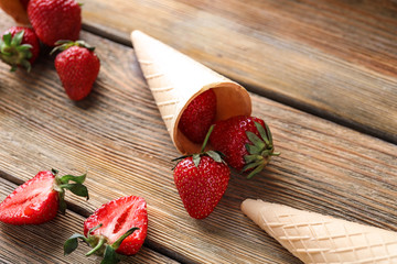 Waffle cones and sweet ripe strawberries on wooden table