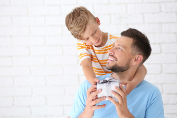 Man receiving gift for Father's Day from his son on light background