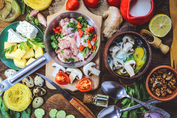 chicken meat in a frying pan with vegetables and mushrooms in batter with egg, herbs and milk. different food ingredients on a wooden background.