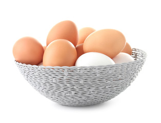 Wicker bowl with chicken eggs on white background