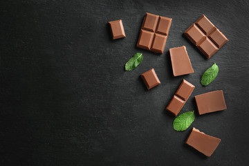 Pieces of tasty milk chocolate and mint leaves on dark background