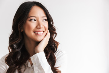 Naklejka premium Image of smiling chinese woman with long dark hair looking aside at copyspace and touching cheek, isolated over white background in studio
