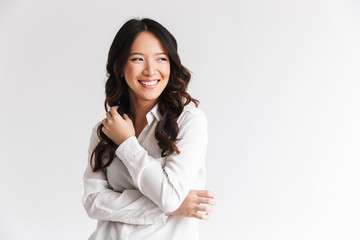 Photo of optimistic asian woman with long dark hair looking aside at copyspace and laughing,...