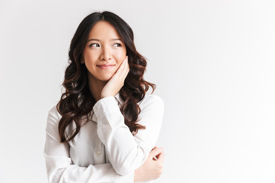 Portrait of happy chinese woman with long dark hair looking aside at copyspace and touching cheek, isolated over white background in studio