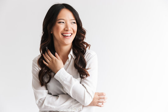 Image of charming chinese woman with long dark hair looking aside at copyspace and laughing, isolated over white background in studio
