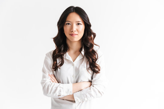 Portrait of beautiful asian woman with long dark hair looking at camera and standing with arms crossed, isolated over white background in studio
