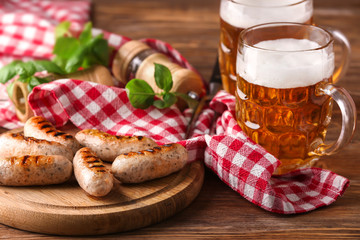 Mugs of delicious beer with grilled sausages and herbs on wooden table