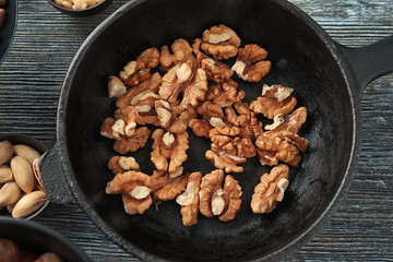 Frying pan with tasty walnuts on wooden table