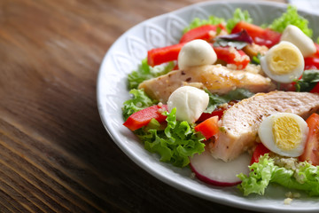 Tasty chicken salad with vegetables and quail eggs in bowl on wooden table