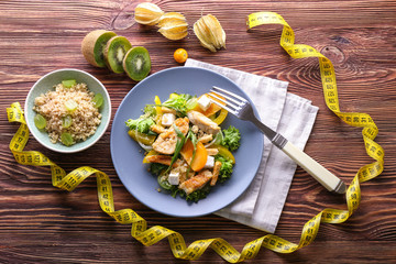 Tasty chicken salad with vegetables and measuring tape on wooden table. Diet food