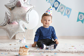 Cute little boy sitting on carpet in room decorated for birthday party