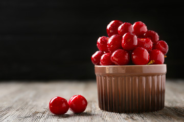 Bowl with tasty cherries on wooden table against dark background