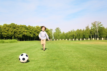 Naklejka premium Cute little boy playing football in park on sunny day