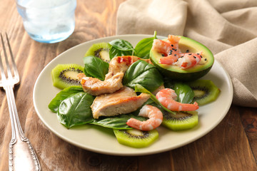 Plate with tasty avocado salad on wooden table