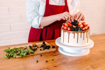 Baker in a red apron decorated with fresh berries and chocolate sponge white cake
