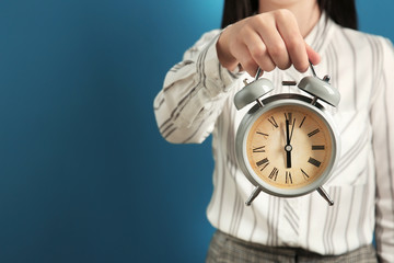 Woman holding alarm clock on color background. Time management concept