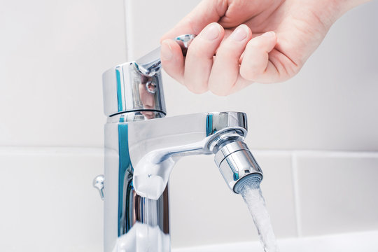 Female Hand On The Handle Of A Chrome Faucet With Running Water