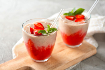 Wooden board with glasses of strawberry smoothie on grey table
