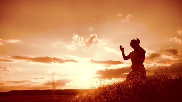 Girl folded her hands in prayer silhouette at sunset. woman praying on her knees lifestyle. slow motion video. Girl folded her hands in prayer pray to God. the girl praying asks forgiveness for sins
