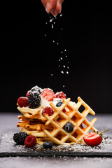 Photo of viennese wafers with raspberries, strawberries sprinkled with powdered sugar on blackboard against blank background