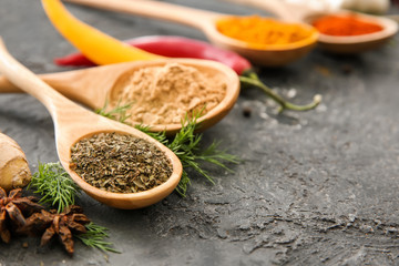 Wooden spoons with different spices on grey background