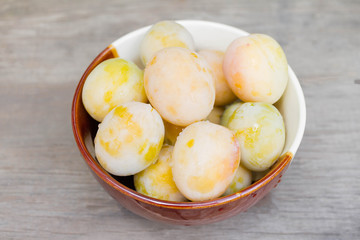 Ripe white plums in a clay bowl on a wooden table. Summer seasonal fruit concept