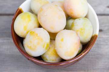 Ripe white plums in a clay bowl on a wooden table. Summer seasonal fruit concept