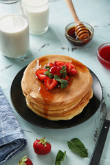 Plate with delicious pancakes, honey and strawberries on table