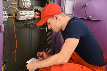 Electrician with house plan near distribution board indoors