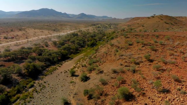 4K aerial view of desert road, mountains and lush green oasis