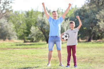 Happy boy and his dad with soccer ball outdoors